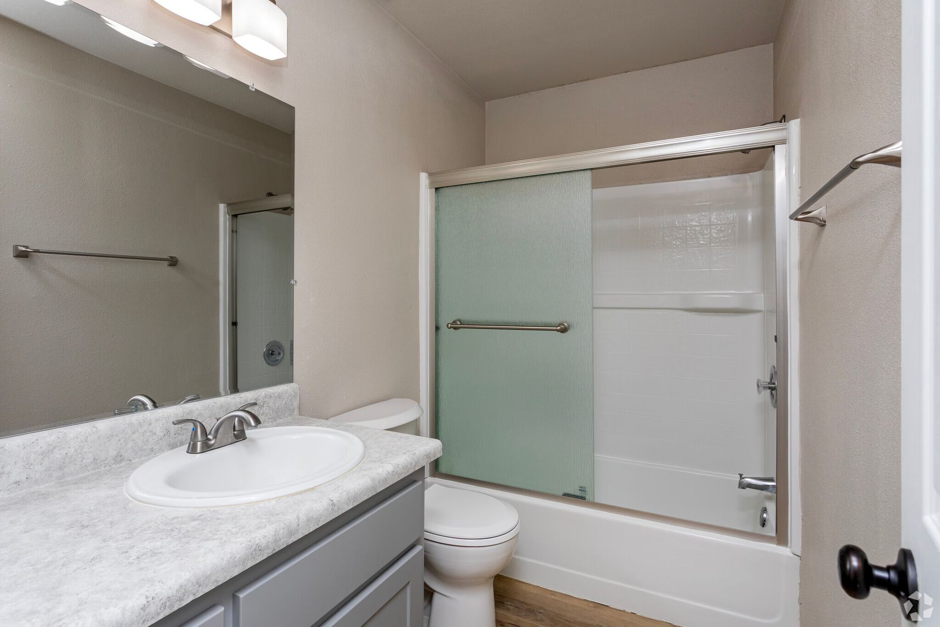 Bathroom with gray vanity, white sink and toilet, and frosted glass shower doors.