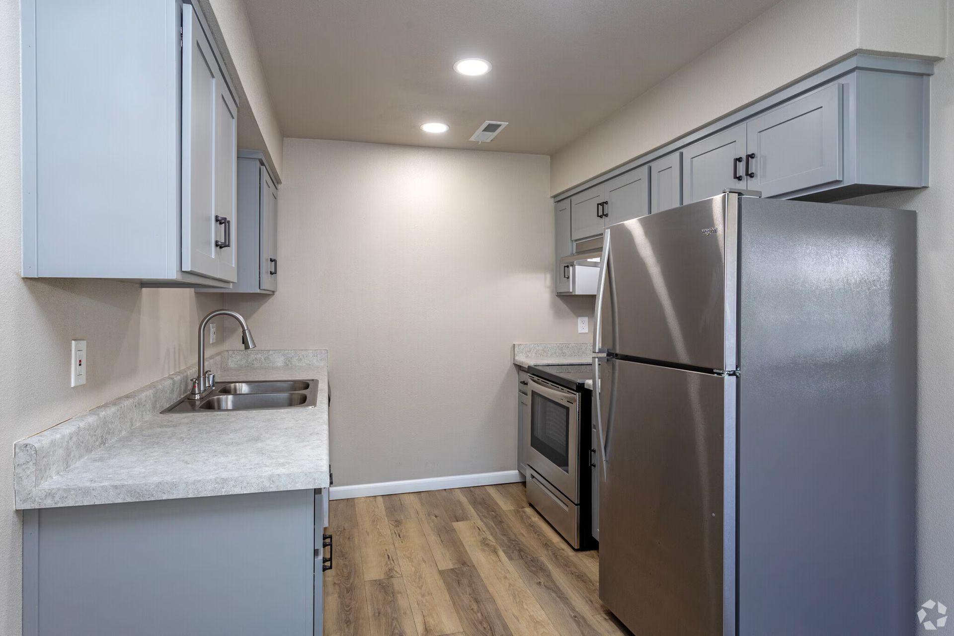 Small kitchen with gray cabinets, stainless steel appliances, and wood-look flooring.