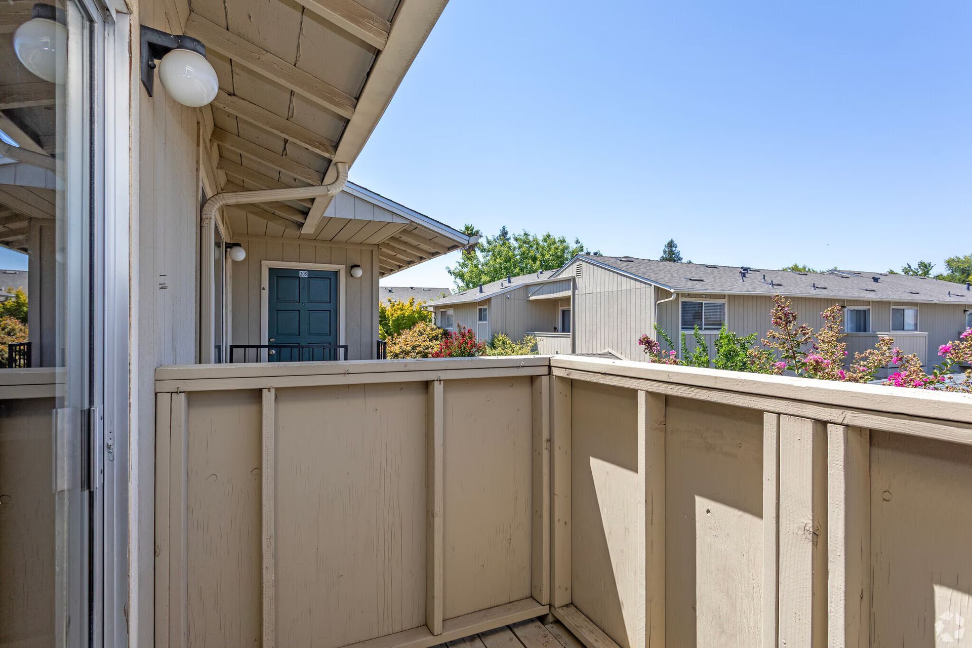 Balcony of an apartment, wooden railing, view of other buildings and blue sky.