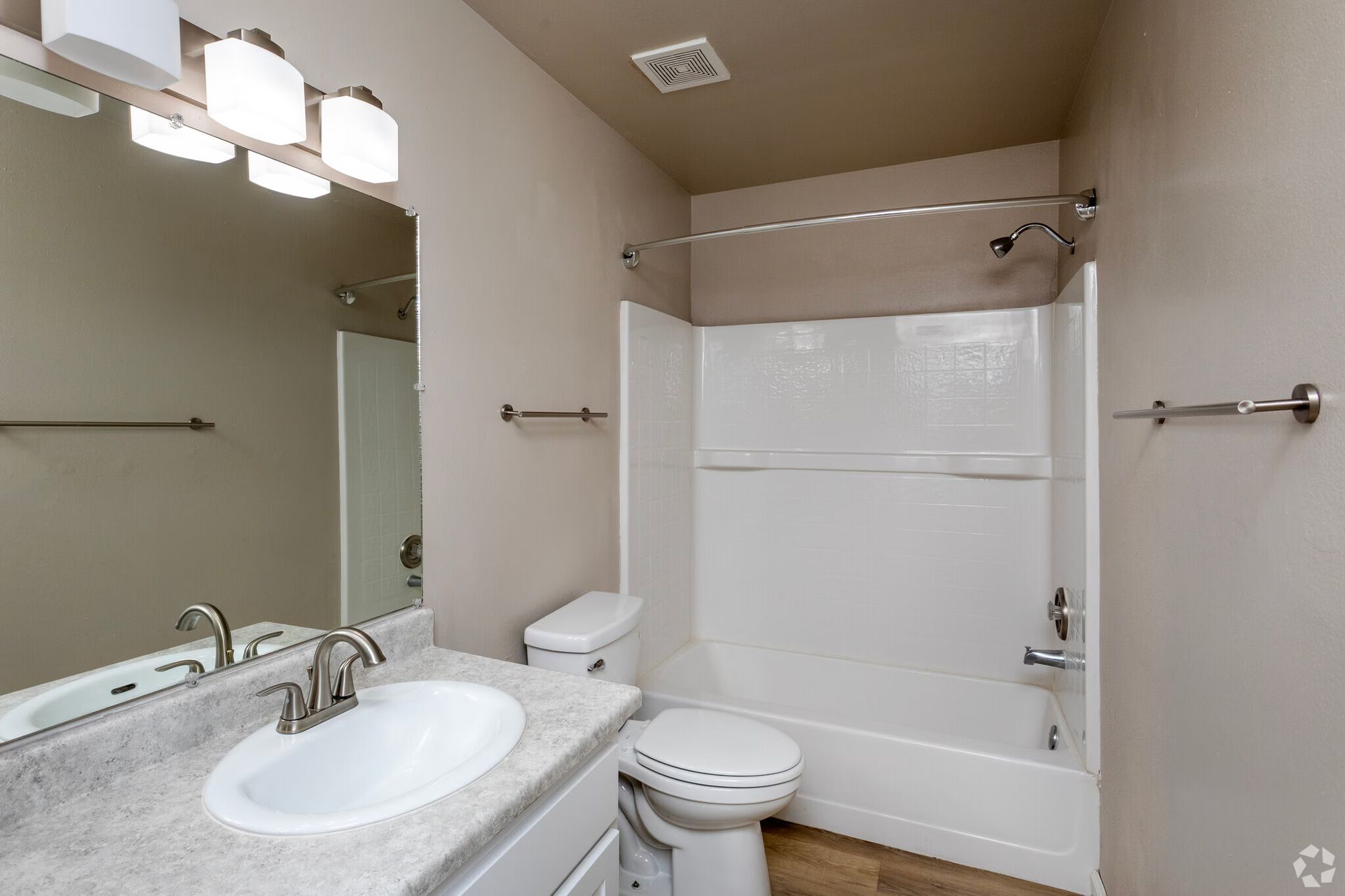 Bathroom with a white toilet, sink, and tub. The walls are neutral colored and there are silver fixtures.