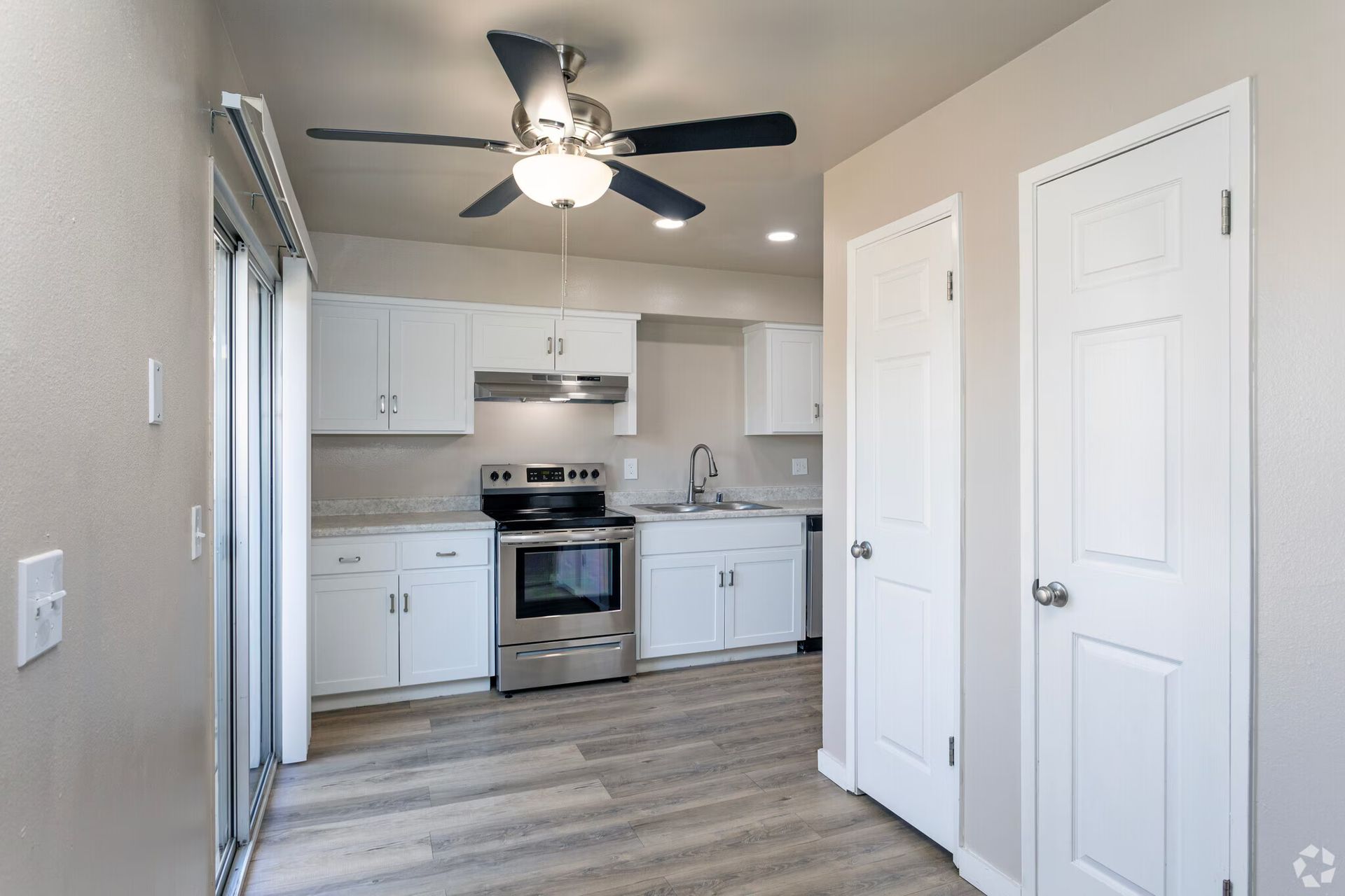 Kitchen with white cabinets, stainless steel appliances, and a ceiling fan. Light wood-look flooring and beige walls.