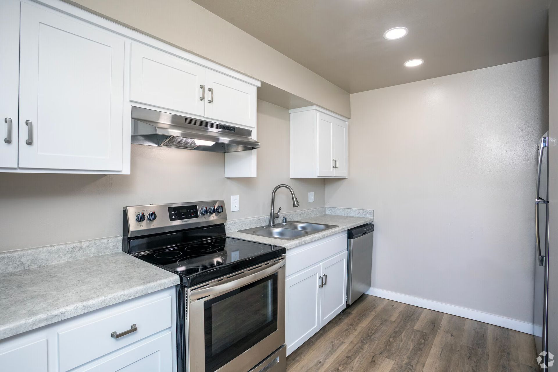 White kitchen with stainless steel appliances, light countertops, and wood-look flooring.