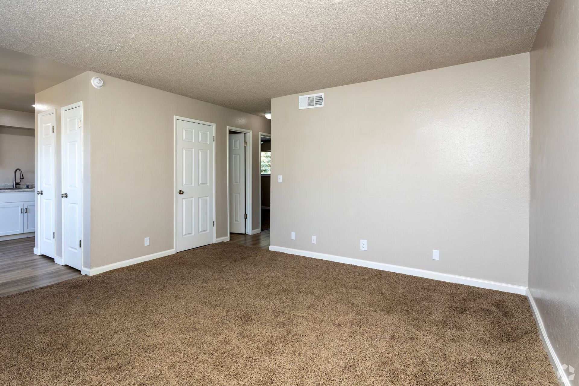 Empty room with brown carpet, tan walls, white doors, and a textured ceiling.