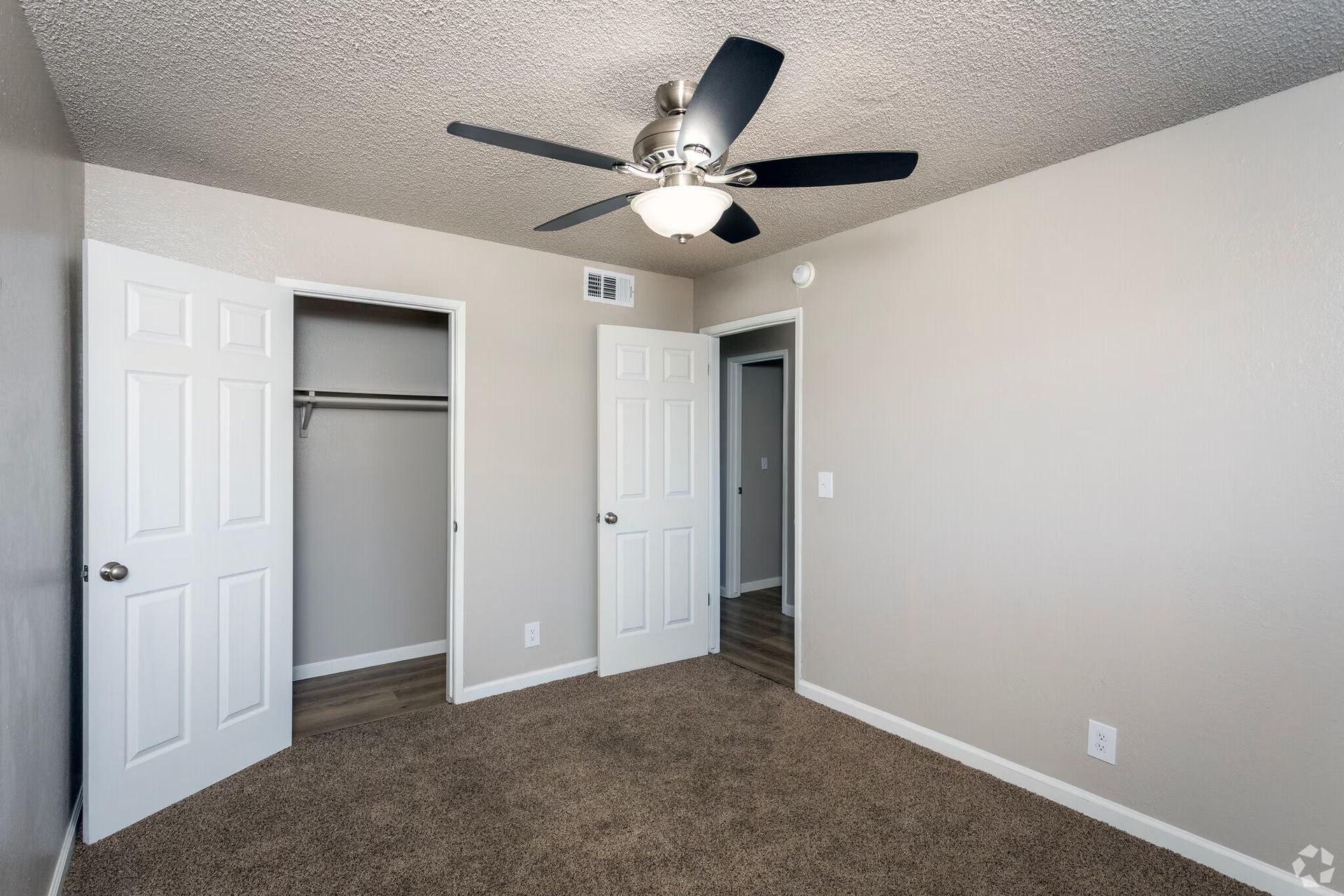 Bedroom with open closet, beige walls, brown carpet, white doors, ceiling fan.