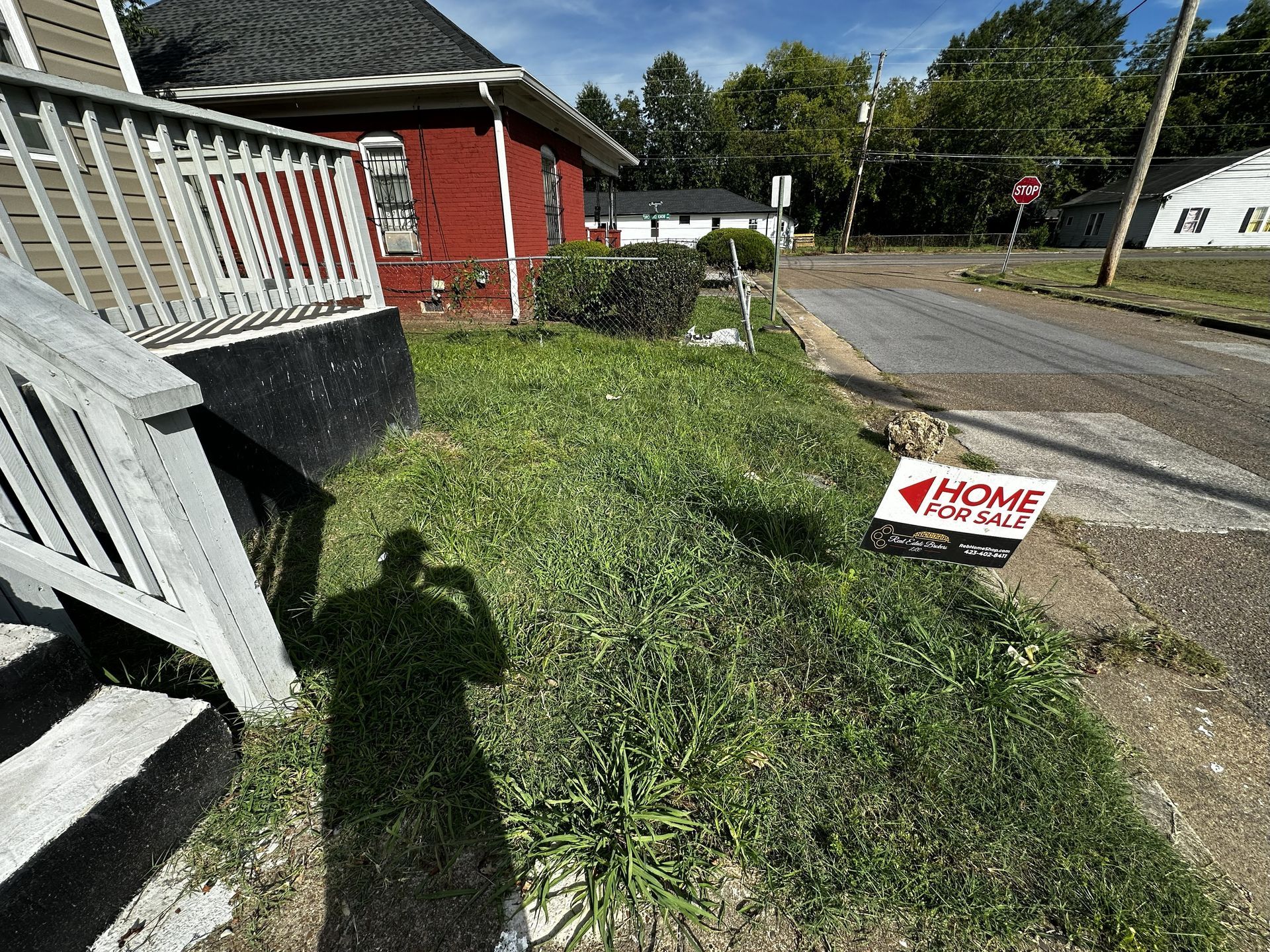 A house for sale with overgrown grass and a "For Sale" sign on the front lawn.