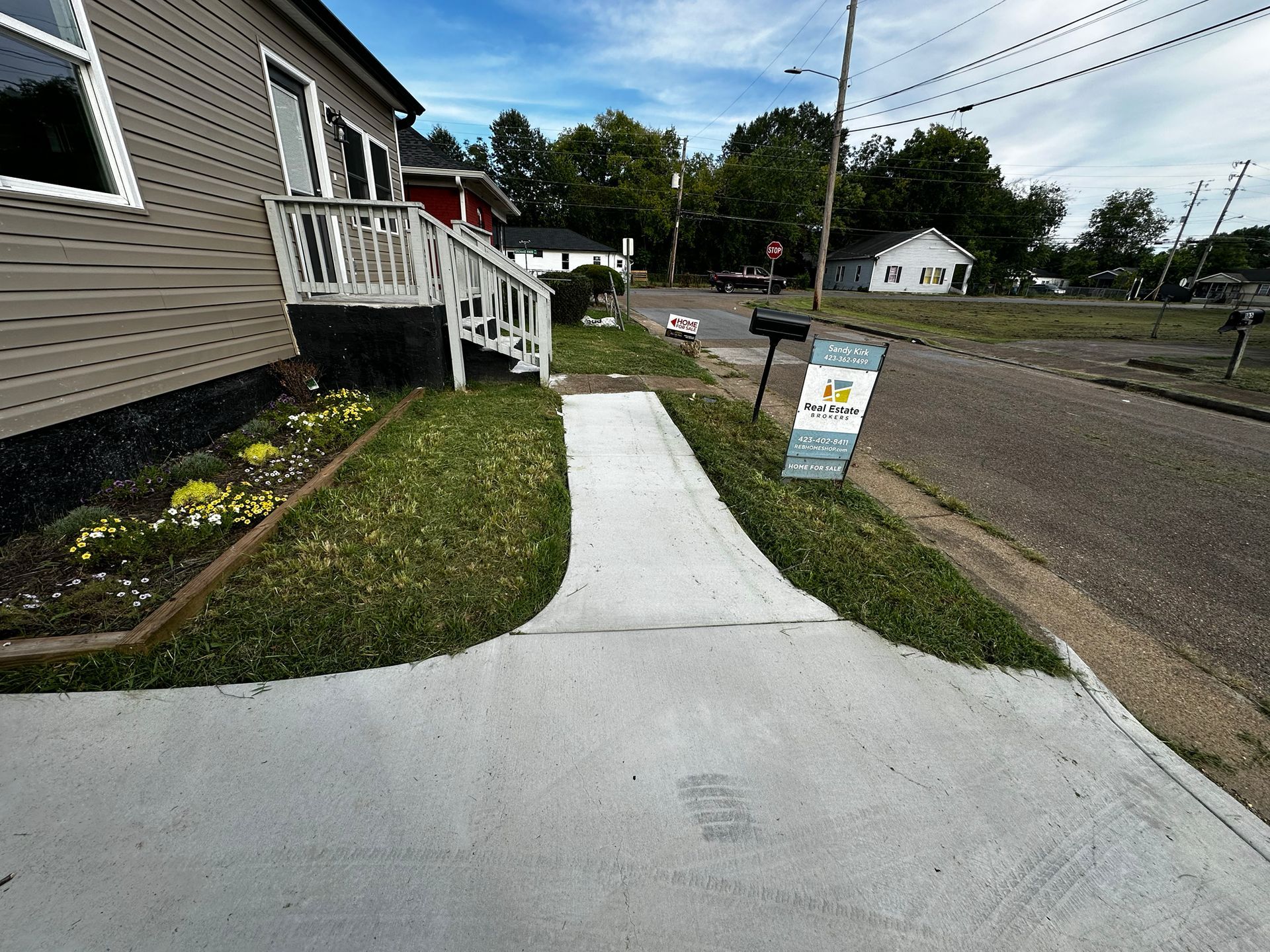 A house with a concrete walkway leading to the front door. Grass and a flower bed are on either side.
