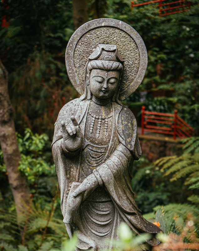 Stone statue of a serene Buddha with halo in a lush, green garden setting.