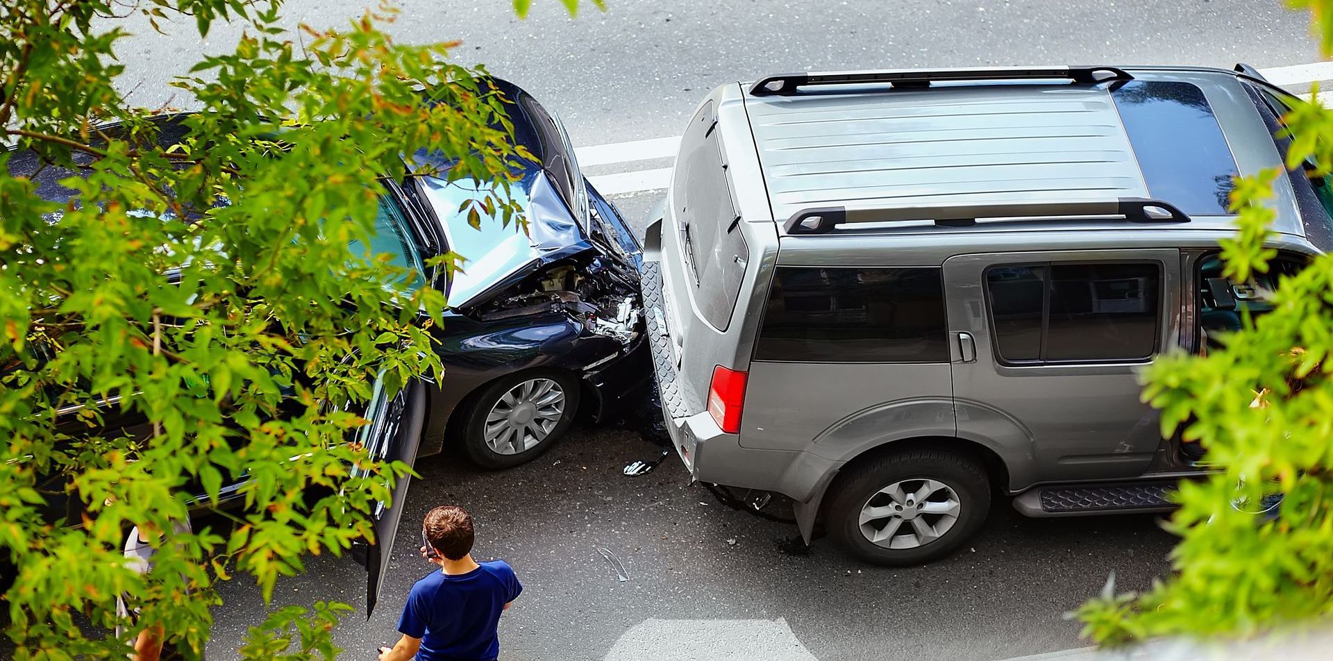 A man is standing next to a car that has crashed into another car.