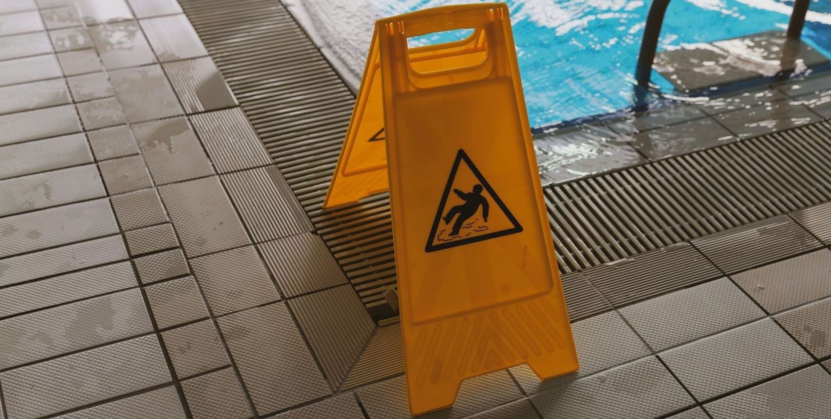 A yellow caution sign is sitting next to a swimming pool.