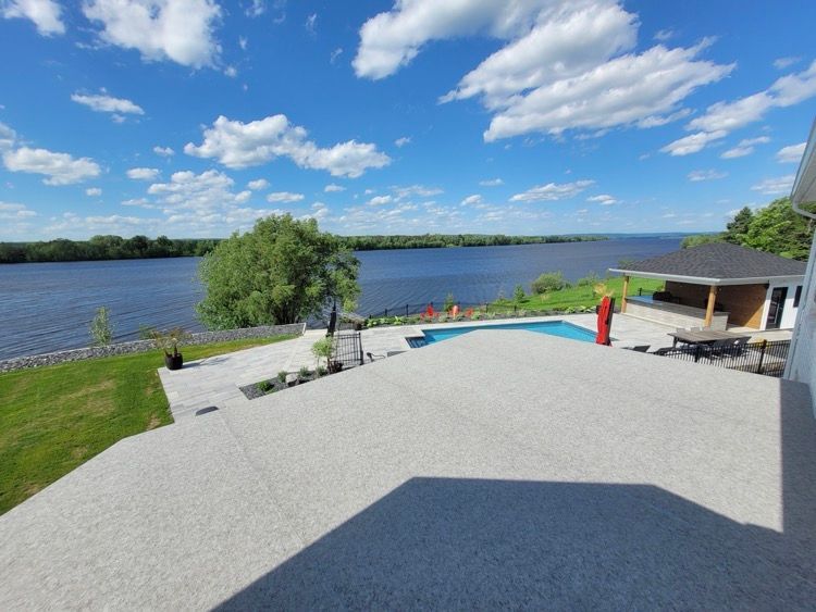 Une grande terrasse grise devant grand plan d'eau.