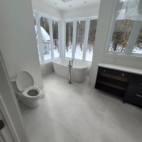 Une salle de bain blanche avec toilettes, baignoire et fenêtre.