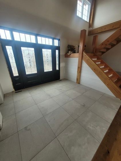 Une pièce vide avec un escalier en bois et une porte noire