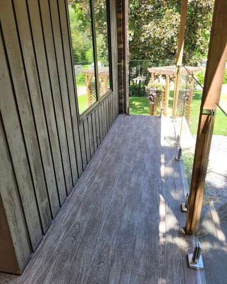 Un porche avec un plancher en membrane de pvc couleurs planche brune et une balustrade en verre.