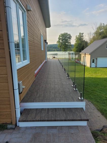 Une terrasse en membrane de pvcavec des escaliers et une balustrade en verre sur le côté d'une maison.