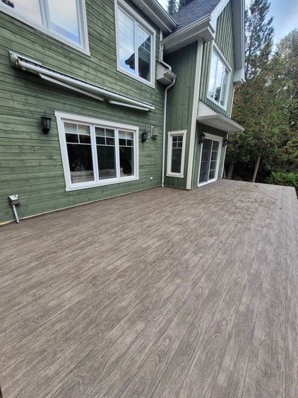 Une grande maison verte avec une terrasse en membrane de pvc devant.