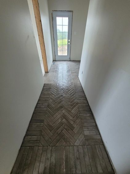 Un couloir avec un motif à chevrons sur le sol et une porte.