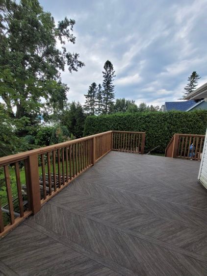 Une grande terrasse en membrane de pvc avec une balustrade en bois entourée d'arbres et d'arbustes.