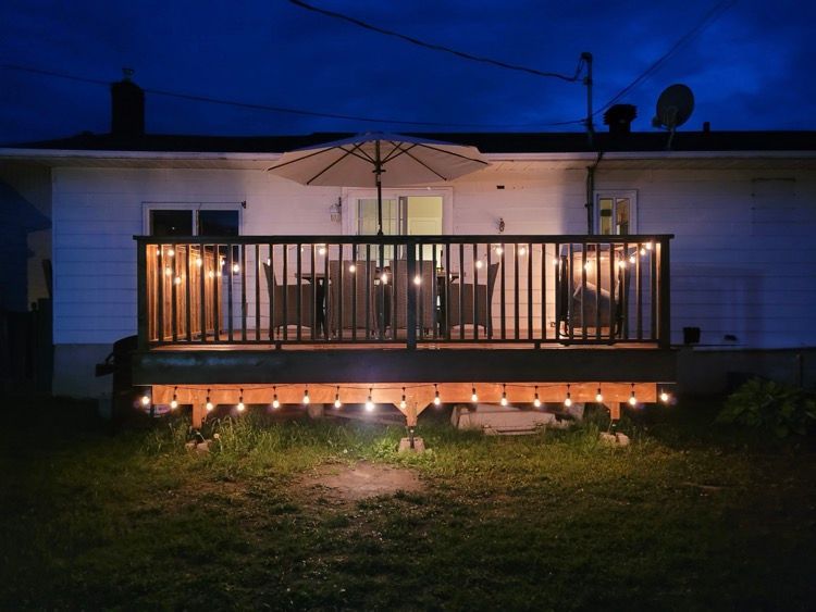 Une terrasse avec des lumières et un parasol est éclairée la nuit.