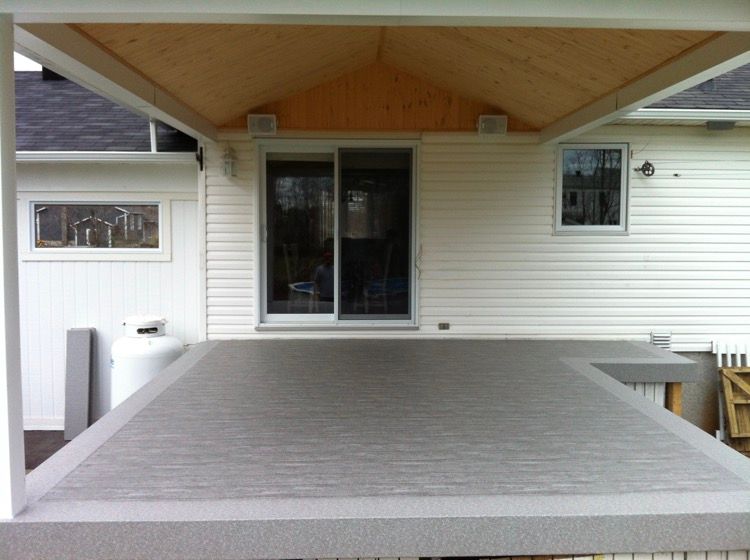 Une maison blanche et beige avec une terrasse en membrane de pvc grise devant.