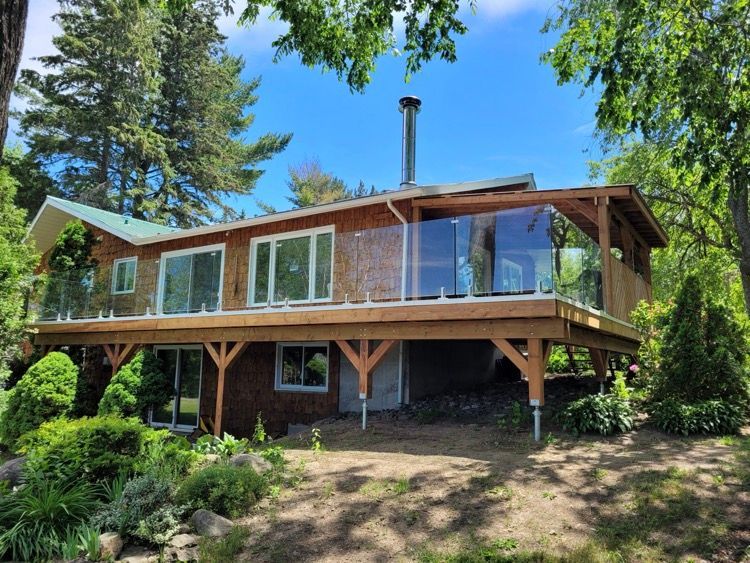 Une maison avec une grande terrasse est entourée d'arbres avec balustrade vitrée.