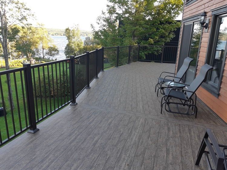 Une grande terrasse avec une rampe noire et des chaises dessus.