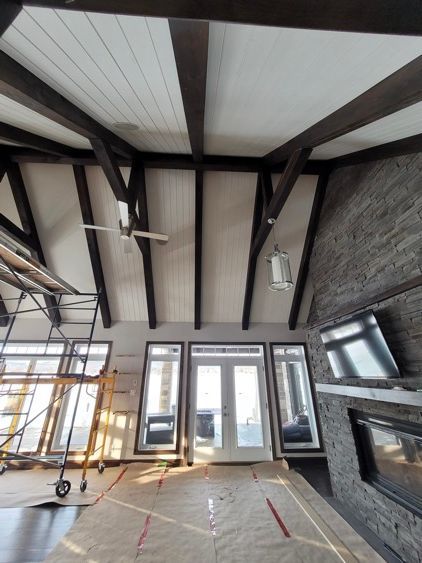 Une grande pièce blanche avec un plafond qui a beaucoup de poutres noires.