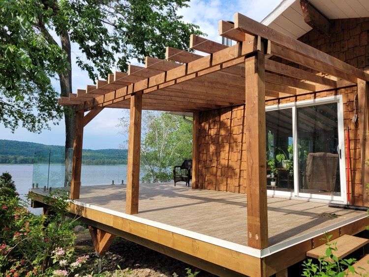 Une terrasse en bois avec une pergola donnant sur un lac.