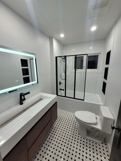 Une salle de bain blanche et noire avec toilette, lavabo, douche et miroir.
