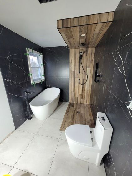 Une salle de bain avec toilette, baignoire et douche avec murs en belle céramique noir avec motifs.