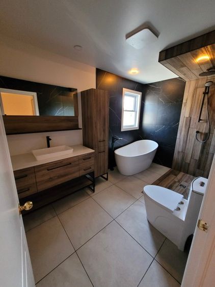 Une salle de bain avec baignoire, lavabo, toilettes, miroir et armoires en bois.