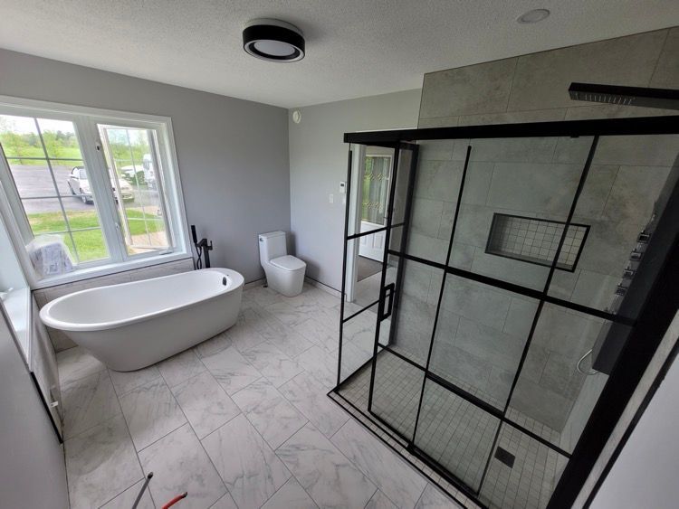 Une salle de bain avec baignoire, toilette, douche et grande fenêtre.