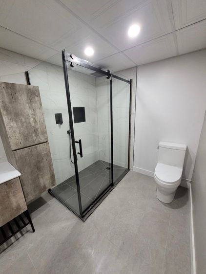 Une salle de bain avec toilette, lavabo et cabine de douche vitrée.