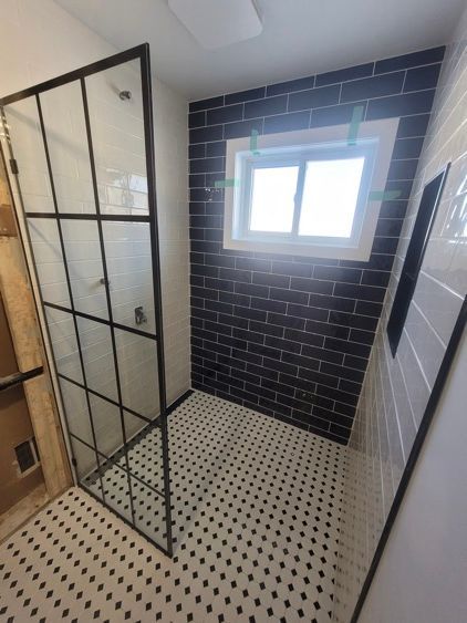 Une salle de bain avec douche à l'italienne et fenêtre avec céramique motifs de briques noires.