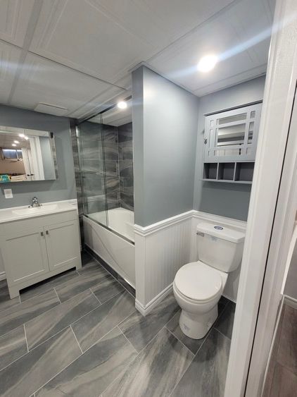 Une salle de bain blanche et grise avec toilette, lavabo, baignoire et miroir.