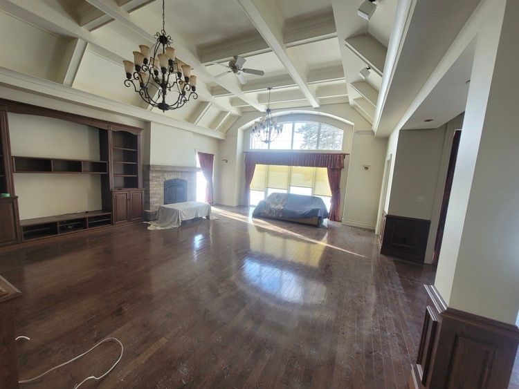 Un salon vide avec du parquet et un lustre suspendu à un plafond architectural.