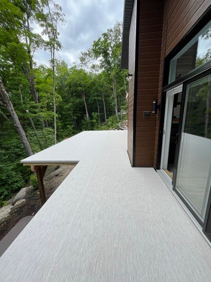 Une terrasse couverte en membrane de pvc avec une porte coulissante en verre et des arbres en arrière-plan.