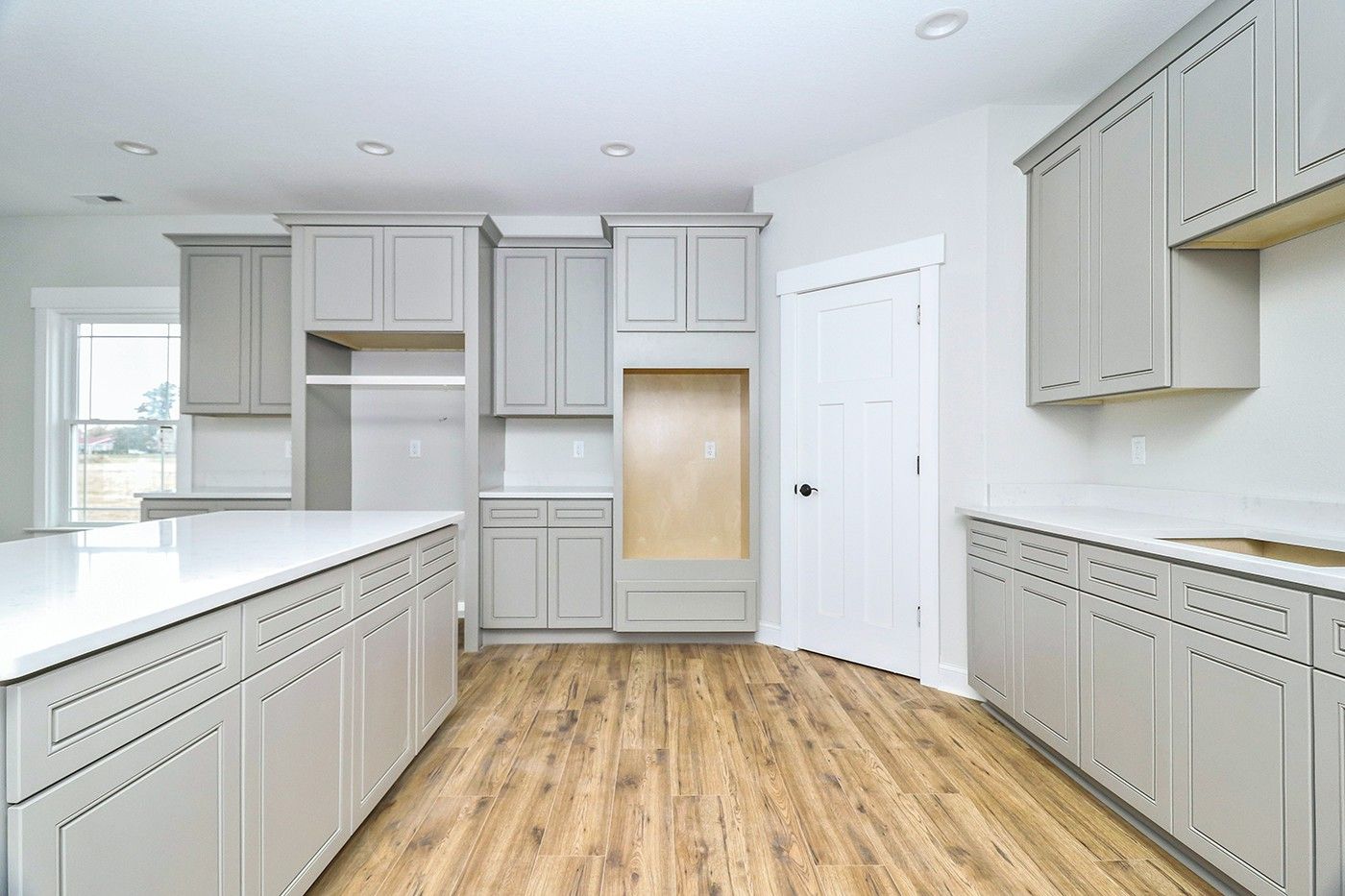 An empty kitchen with gray cabinets and wooden floors.