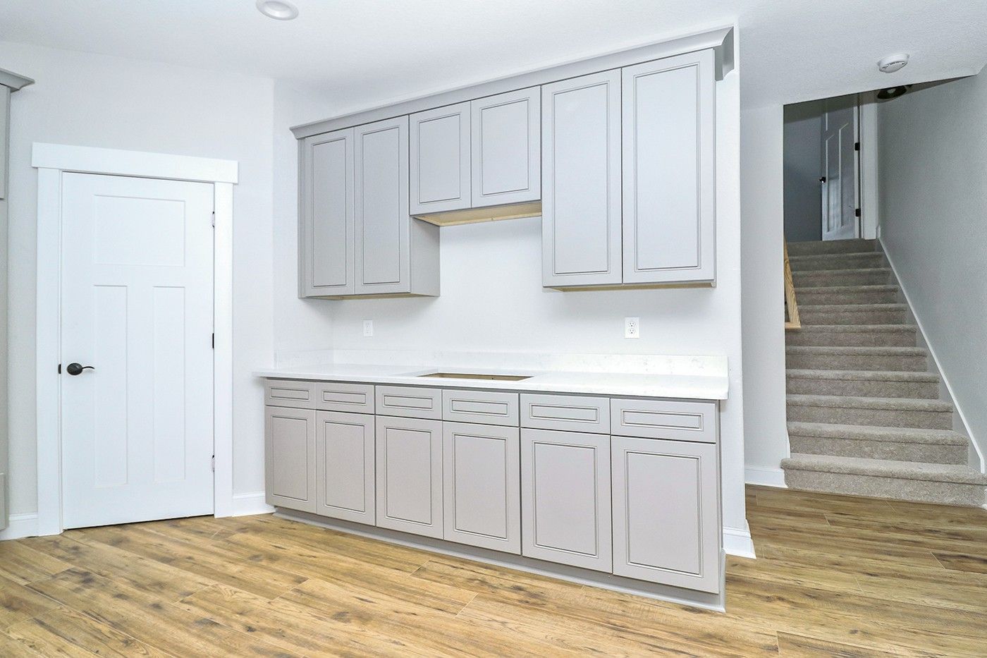 A kitchen with gray cabinets and hardwood floors in a basement with stairs.