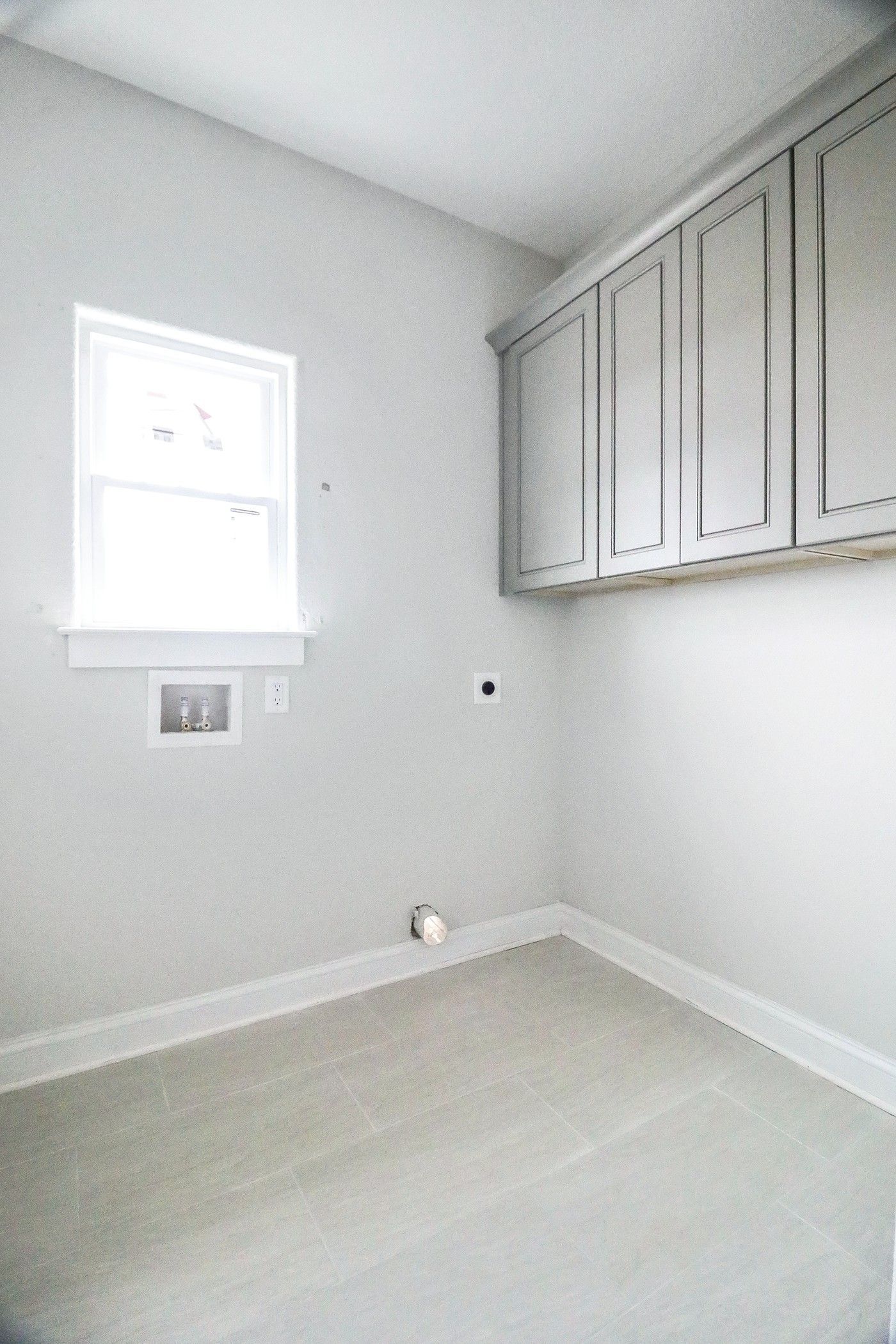 An empty laundry room with a window and cabinets.