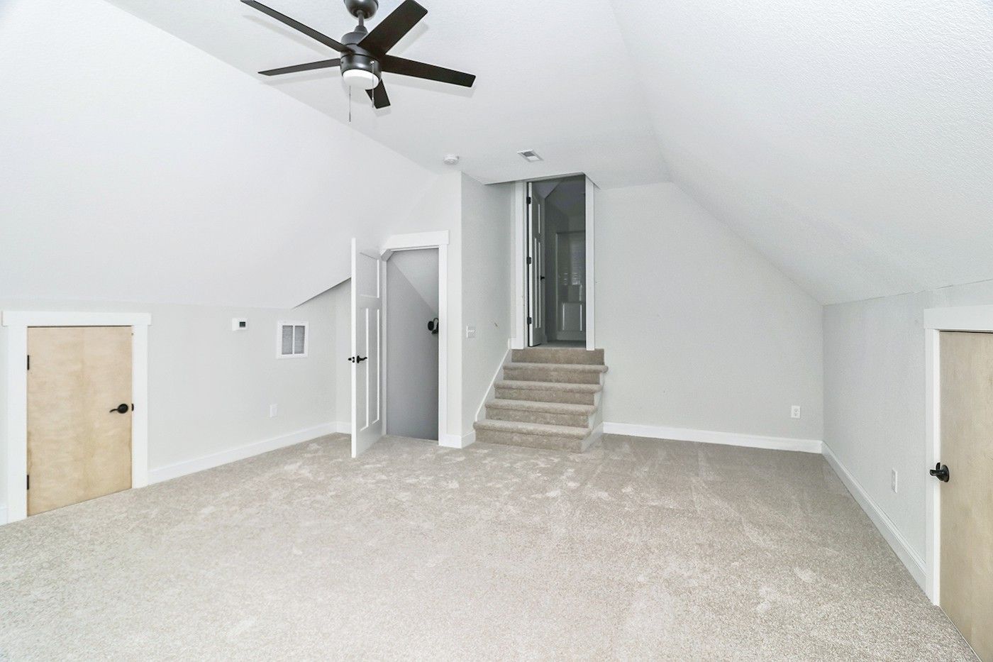 An empty room with a ceiling fan and stairs leading up to the second floor.