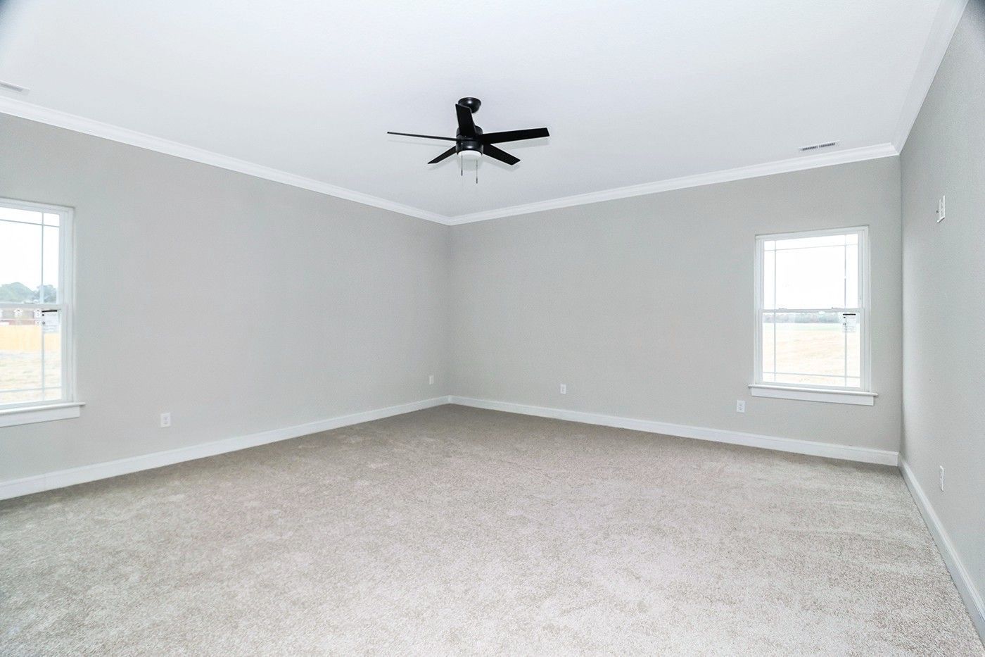 An empty bedroom with a ceiling fan and two windows.