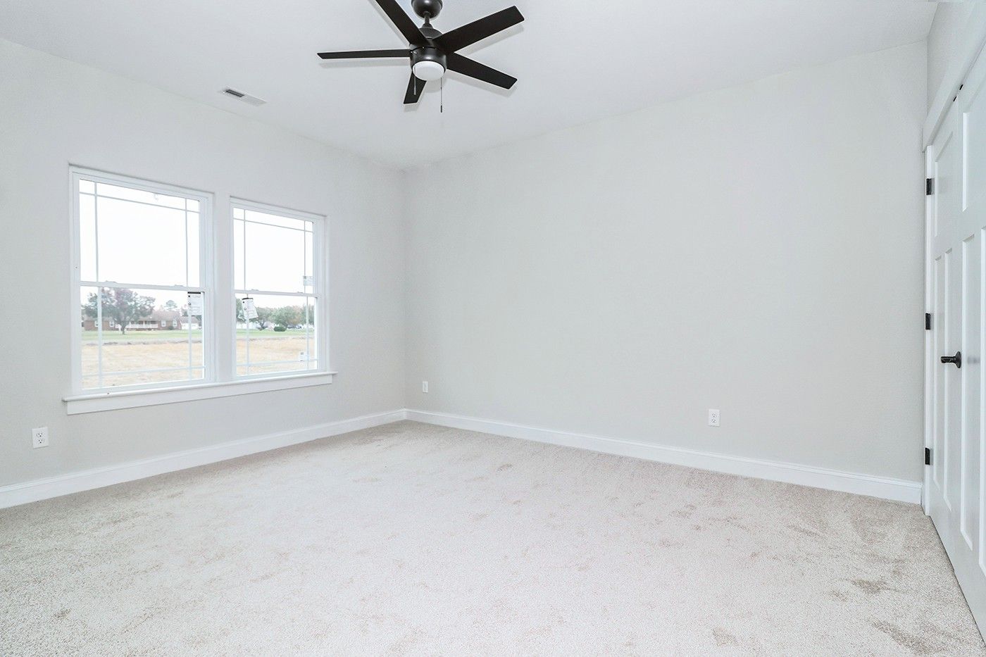 An empty bedroom with a ceiling fan and two windows.