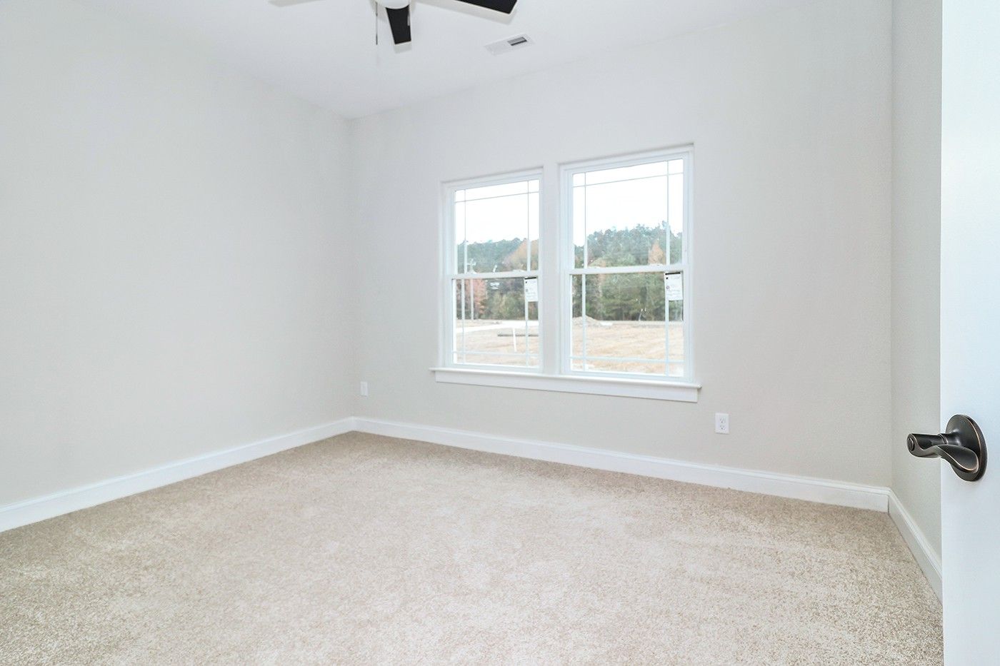 An empty bedroom with two windows and a ceiling fan.