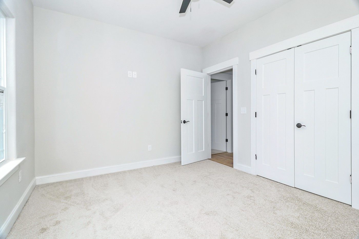 An empty bedroom with white walls and a ceiling fan.