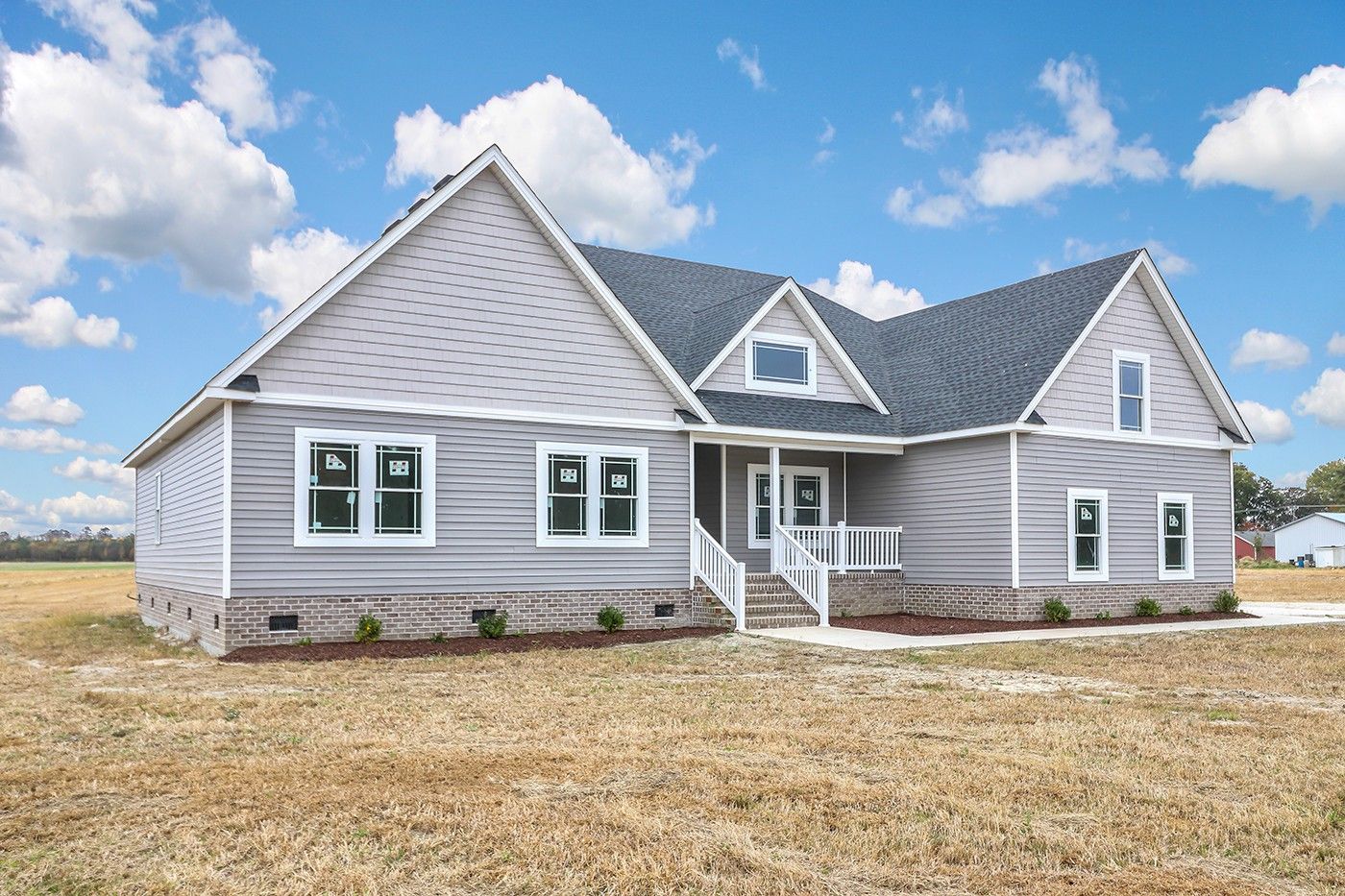 A large gray house with a gray roof is sitting in the middle of a field.