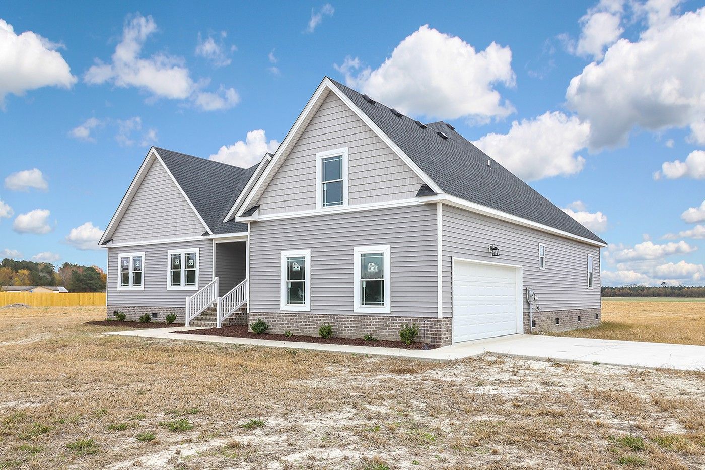 A large gray house with a garage in the middle of a field.