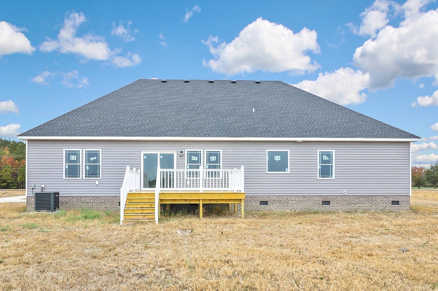 The back of a house with a large deck in a field.