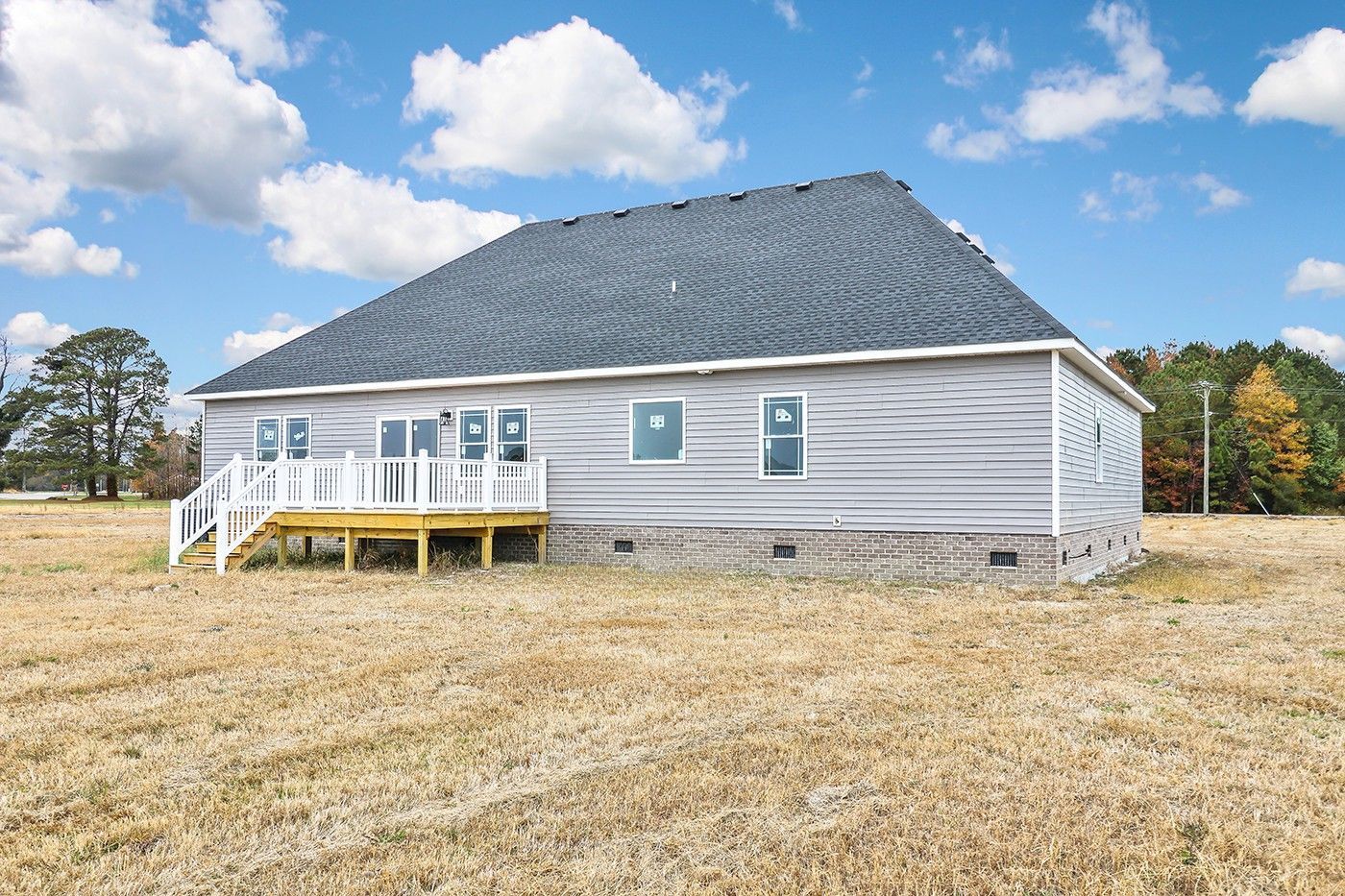 The back of a house with a deck and stairs in a field.