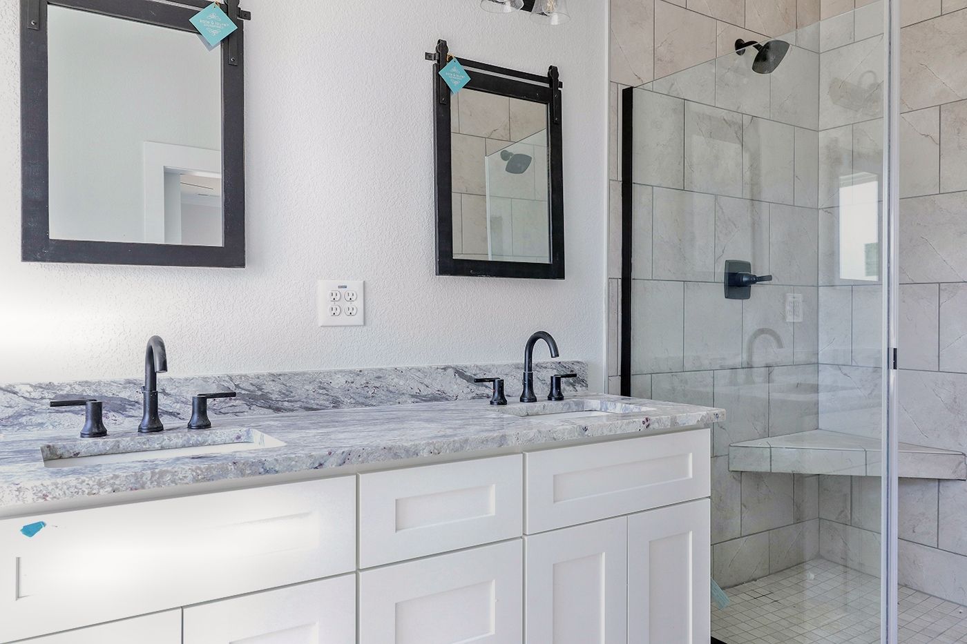 A bathroom with two sinks , two mirrors and a walk in shower.