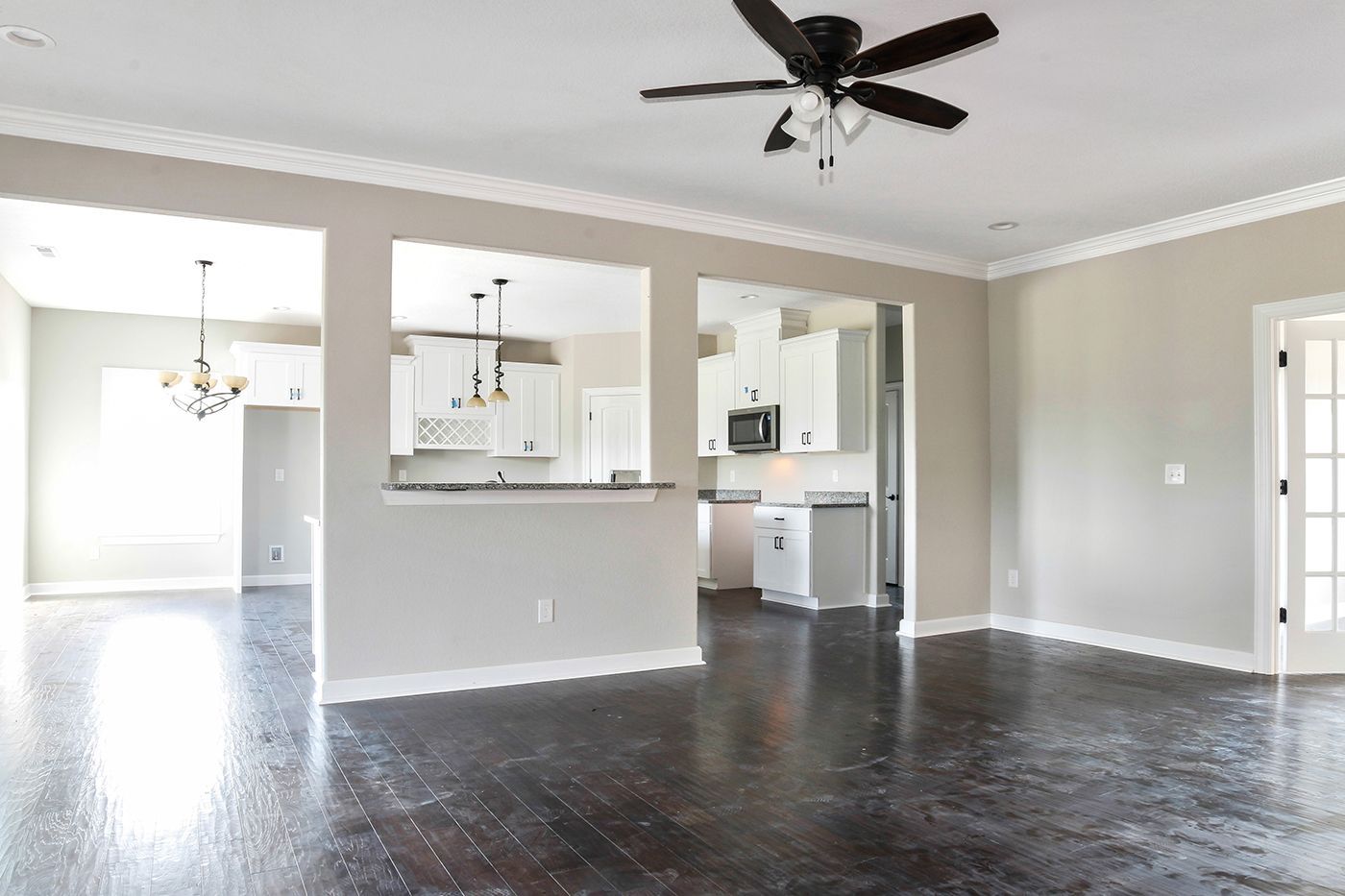 A living room with a ceiling fan and a kitchen in the background.